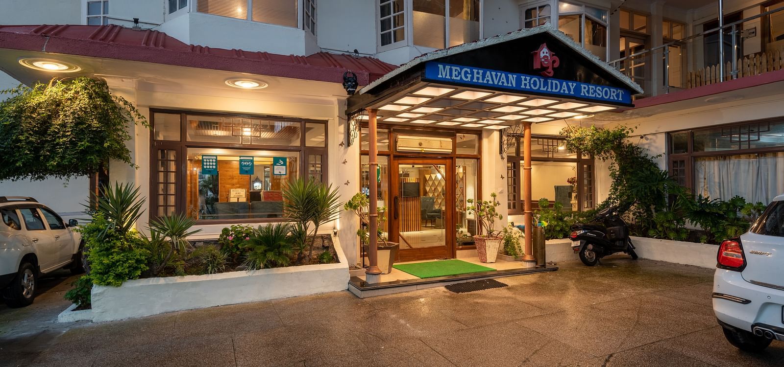 A photo of the entrance to DLS Meghavan Resort, showing the building's facade, entrance way, and some potted plants.